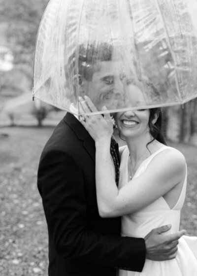 Black and white portrait of a smiling couple under an umbrella, at their airbnb elopement, upstate in the fall.
