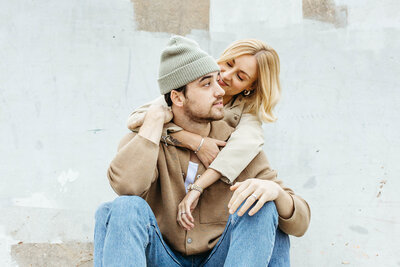 Editorial engagement photo of couple sitting close together, laughing in natural light.