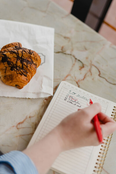 Anna Bradshaw writing in a notebook next to a pastry on the table
