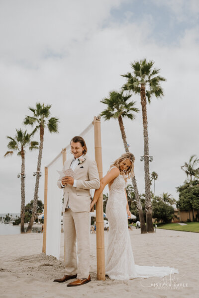 bride and groom standing on a beach with palm trees in the background