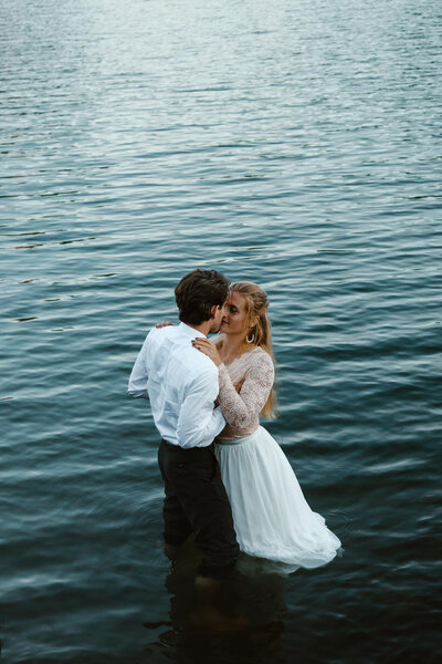 after eloping in washington state, a bride and groom kiss in icy blue waters