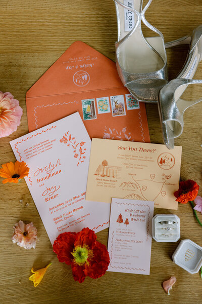 Customized calligraphy flat lay featuring wedding invitations, envelopes, flowers and more represent full service design by Life in Letters.