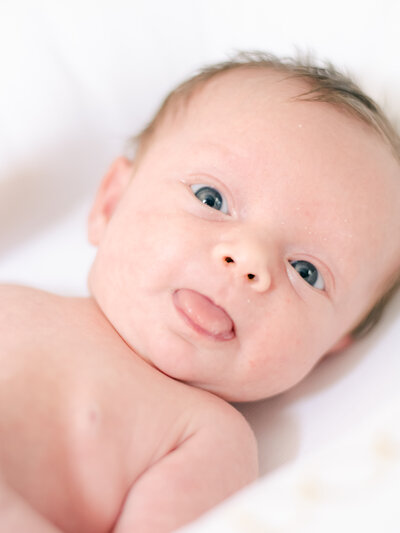 Newborn. baby girl poking er tongue out at camera while in her Richmond nursery.