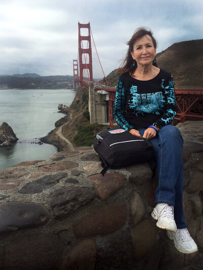 Charlotte Meares, author, ghostwriter,  editor, publisher, seated on a stone wall with the Golden Gate bridge in the background.