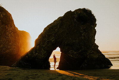 Environmental portrait of omen standing in rock archway with sunset light streaming through