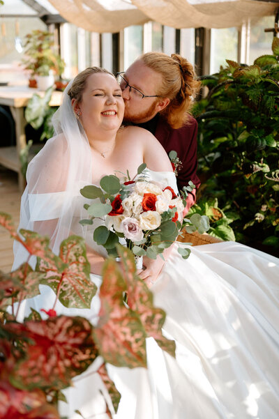 Bride giggling while being kissed by her groom in an outdoor setting