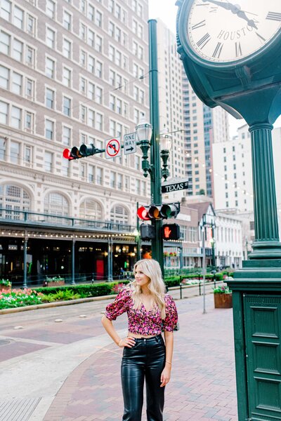 Portrait of a girl in a floral top and leather pants posing on a city street with a building behind her