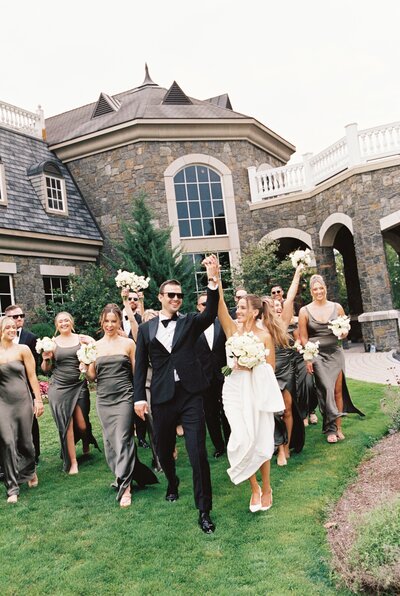 A stylish wedding party walks confidently across the lush grounds of Saratoga National Golf Course, with the bride and groom leading the way in a modern, high-fashion wedding celebration.