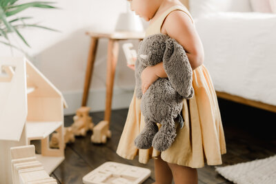 A baby sits on a soft mat surrounded by neutral wooden toys, chewing thoughtfully on a block – Family Autism Support Coach at Chantal Hewitt Coaching