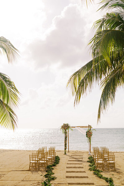 Beach wedding venue setup with golden chairs and palm trees framing a seaside ceremony altar.