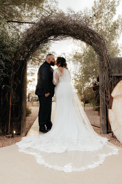 Bride and groom kiss underneath  an arch in gilbert Arizona
