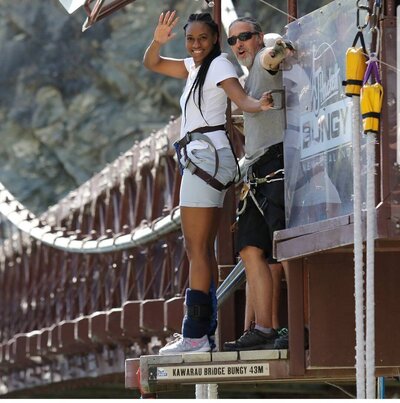 Nadia Forte waves before taking a thrilling bungy jump off the Kawarau Gorge Suspension Bridge in New Zealand. Experience bespoke adventure travel, adrenaline-filled excursions, and high-touch luxury itineraries.