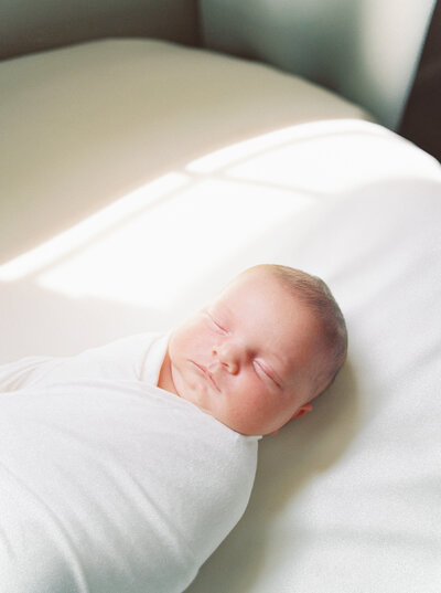 Baby boy wrapped in tight white swaddle sleeps on a white background