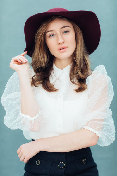 Model in Modest outfit of purple hat and white blouse posing in Glass Darkly studio in Los Angeles