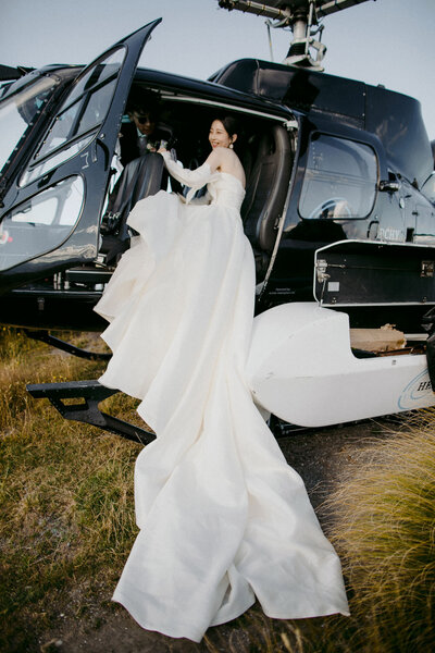 Bride in huge dress climbing into helicopter on mountaintop