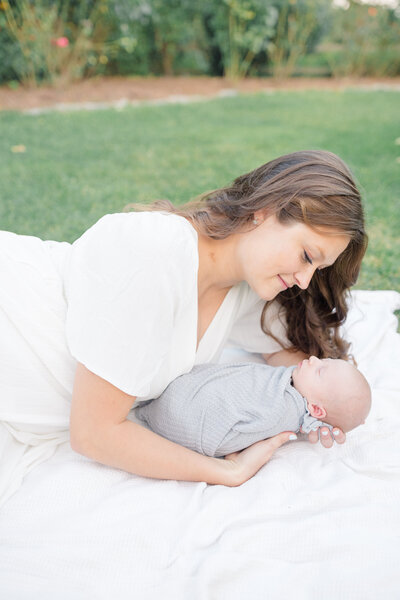 Newborn session in Connecticut with mother and father lovingly holding their newborn baby. The parents gaze at their child with deep affection, surrounded by a peaceful, natural setting