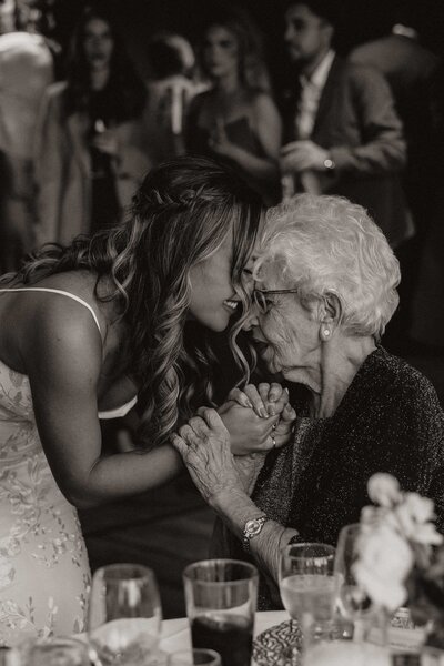 Black and white photo of a bride holding hands with her grandmother, leaning in as they share a close, emotional moment