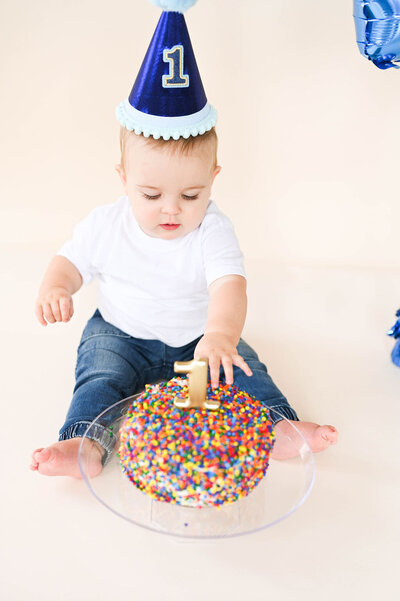 A small child in a birthday hat reaching out towards a cake.