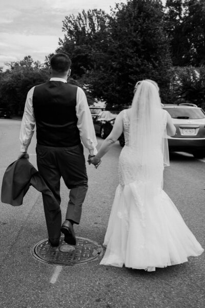 A happy bride and groom walk hand in hand through a scenic backyard setting during their wedding in Dumfries, Virginia, capturing a joyful candid moment by Quinn Photography LLC.
