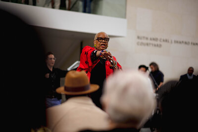 A woman in a red  points to a crowd at the Museum of Fine Arts, Boston.