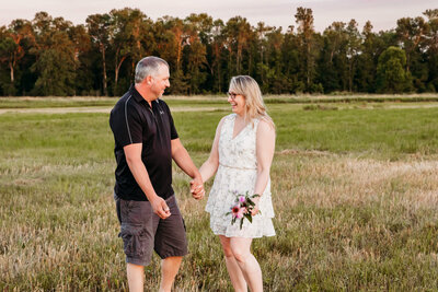 couple dancing in a field together while holding flowers for engagement session