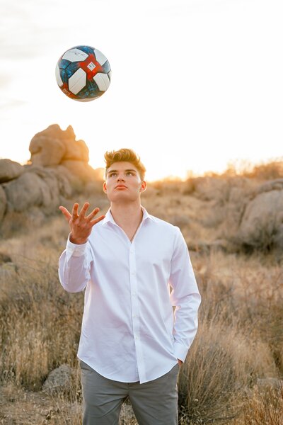 senior boy in the arizona desert tossing soccer ball up into air 