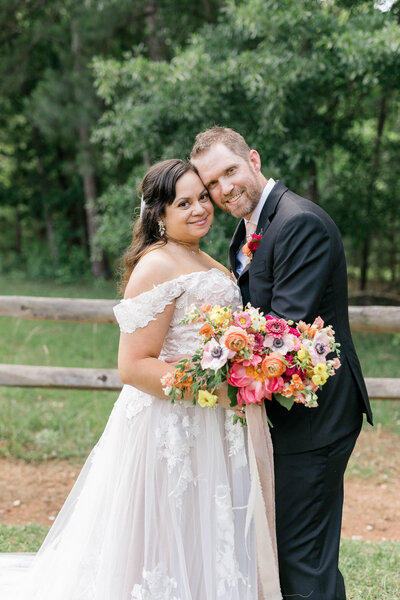A bride and groom in Atlanta with their arms around each other, cheek to cheek, smiling at the camera. The bride is holding a colorful bouquet with long pink ribbons hanging from the stems.