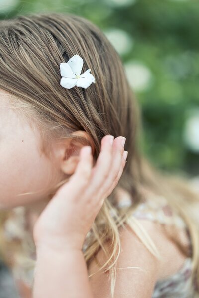 A candid moment of a little girl putting a flower in her hair.