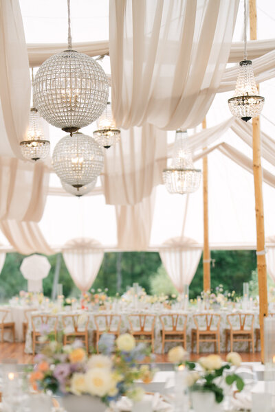Outdoor wedding tablescape with crystal glassware, fine china, blue and white tablecloth and a pink floral arrangement