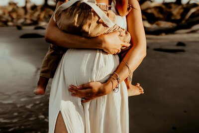An expectant mother radiates beauty in a rust orange boho dress, gently looking down and cradling her belly. This captivating moment is skillfully captured by Fire Family Photographer, a talented maternity photographer from Macon, GA.