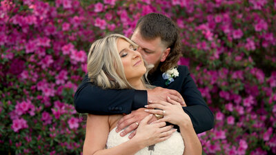Couple embracing each other in front of vibrant pink flowers during their wedding portrait session.