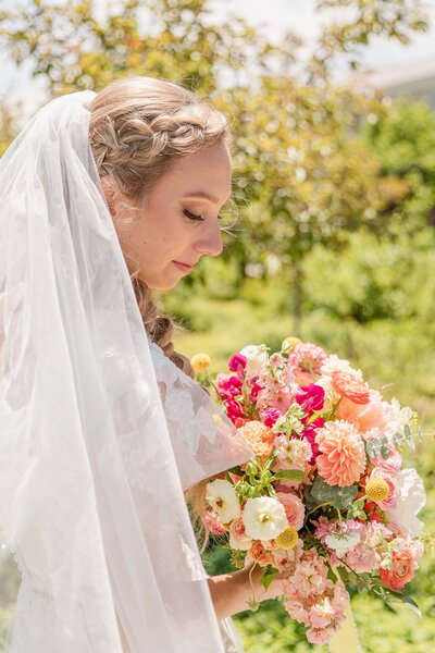 Beautiful bride in wedding dress and veil holding a colorful bouquet at outdoor bridal shoot.