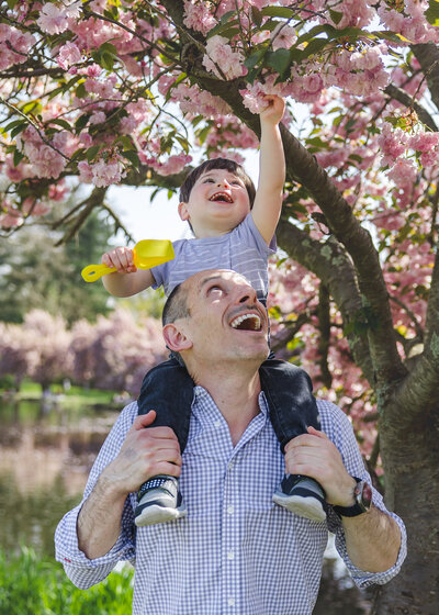 Lifestyle photo of laughing son on father's shoulders at an Essex County, New Jersey park in the fall.