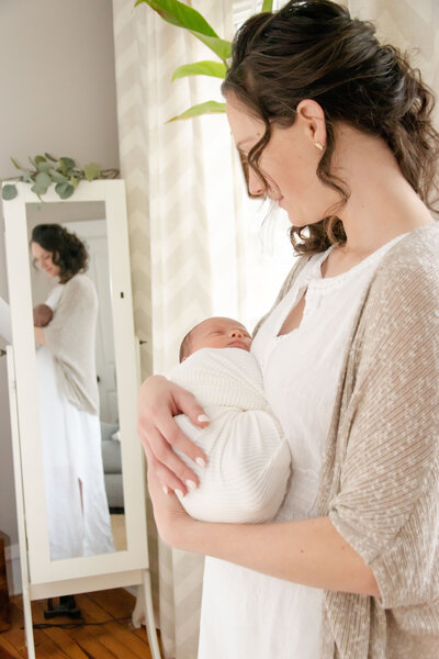 Mom holding her newborn baby in front of mirror.