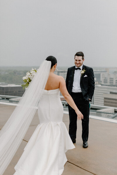 A wedding couple smiling at each other on a rooftop during their first look 