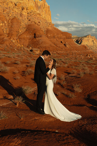 A groom who is delicately holding the face of his bride in the middle of Captiol Reef National Park. The red rock and buttes are surrounding them.