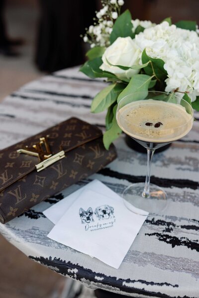 espresso martini, louis vuitton clutch, and custom bar napkins styled on table