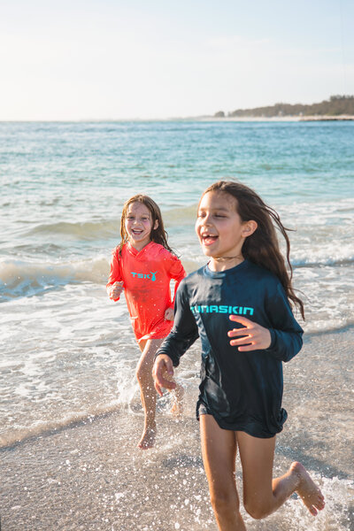 Two girls run on the beach wearing protective clothing made of sustainable fabric