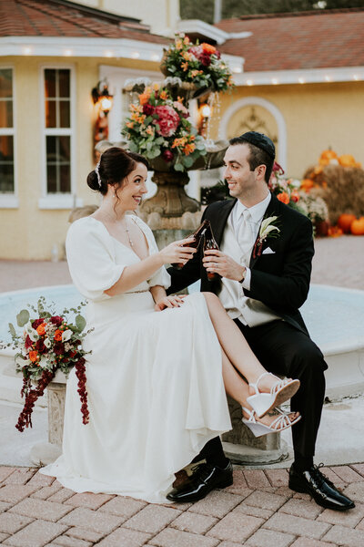 Bride and groom toast beer bottles in front of floral fountain at romantic Casa Lantana Brandon FL wedding