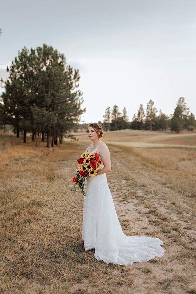 Brunette wedding bride with white dress and red and yellow flowers. Smiling to the side. Captured by Michelle Betz Photography