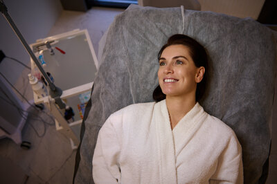 overhead-view-darkhaired-beautiful-caucasian-woman-white-bathrobe-smiling-with-beautiful-toothy-smile-lying-massage-couch-while-receiving-beauty-treatment-wellne