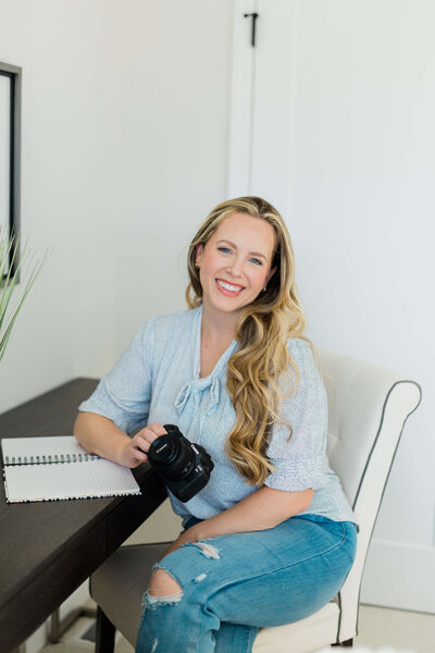 happy woman sitting in chair at desk with a camera and smiling