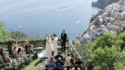 A beautiful Positano seaside wedding ceremony of Sarah and Zach, featuring the couple exchanging vows with the turquoise sea and scenic cliffs as a backdrop.