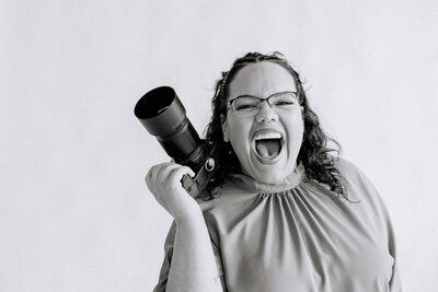 Black and white photo of a person smiling with a camera in one hand