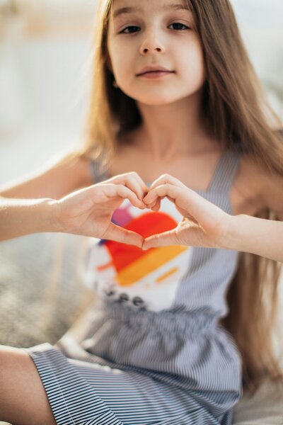 Young girl making a heart hand gesture | symbol of connection and family support at Rooted Within