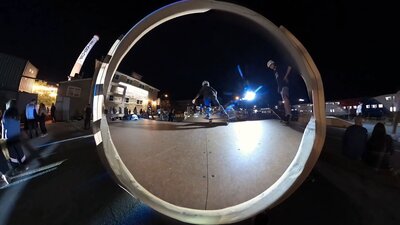 Skateboarders performing tricks through a large circular ramp during nighttime event video production