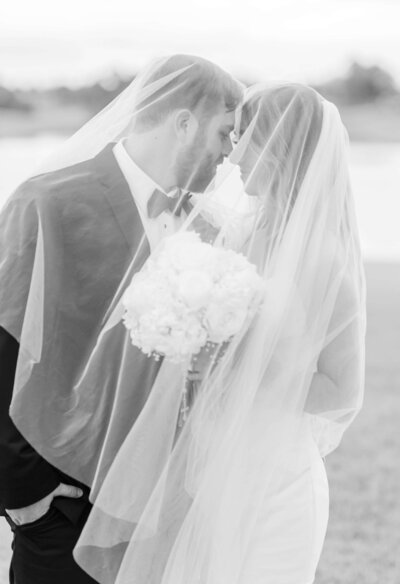 Black and white phoot of bride and groom under veil