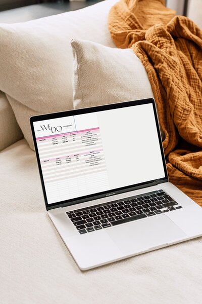 Mockup image of a laptop on a couch with an orange blanket in the background. On the laptop screen, is the hair/makeup schedule spreadsheet