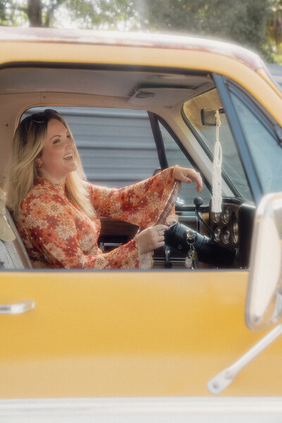 woman laughs in driver's seat of vintage yellow truck