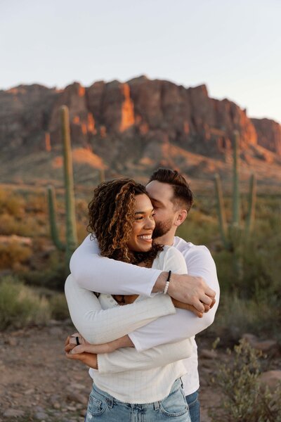 Man hugs woman from behind and they tangle arms together for engagement photos
